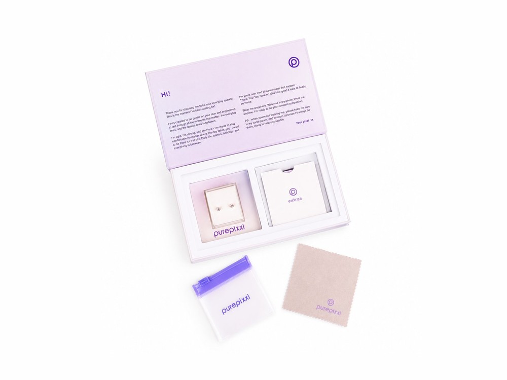 A purepixxi gift box opened, showing the welcome card, a pair of earrings, the pouch and the cleaning cloth.
